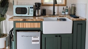 A compact kitchen with a microwave, coffee maker, and a refrigerator. There is a window above the sink, and shelves above the counter. - The Getaway · Cozy cabin, Hot tub, Outdoor shower (Valley Mills)