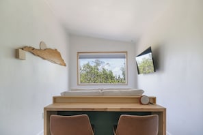 A room with a bed, a desk, a chair, a window with a view of trees, and a mounted TV.