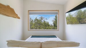 A bedroom with a bed, a window with a view of trees, and a wall-mounted piece of art. - The Getaway · Cozy cabin, Hot tub, Outdoor shower (Valley Mills)