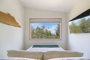 A bedroom with a bed, a window with a view of trees, and a wall-mounted piece of art. - The Getaway · Cozy cabin, Hot tub, Outdoor shower (Valley Mills)