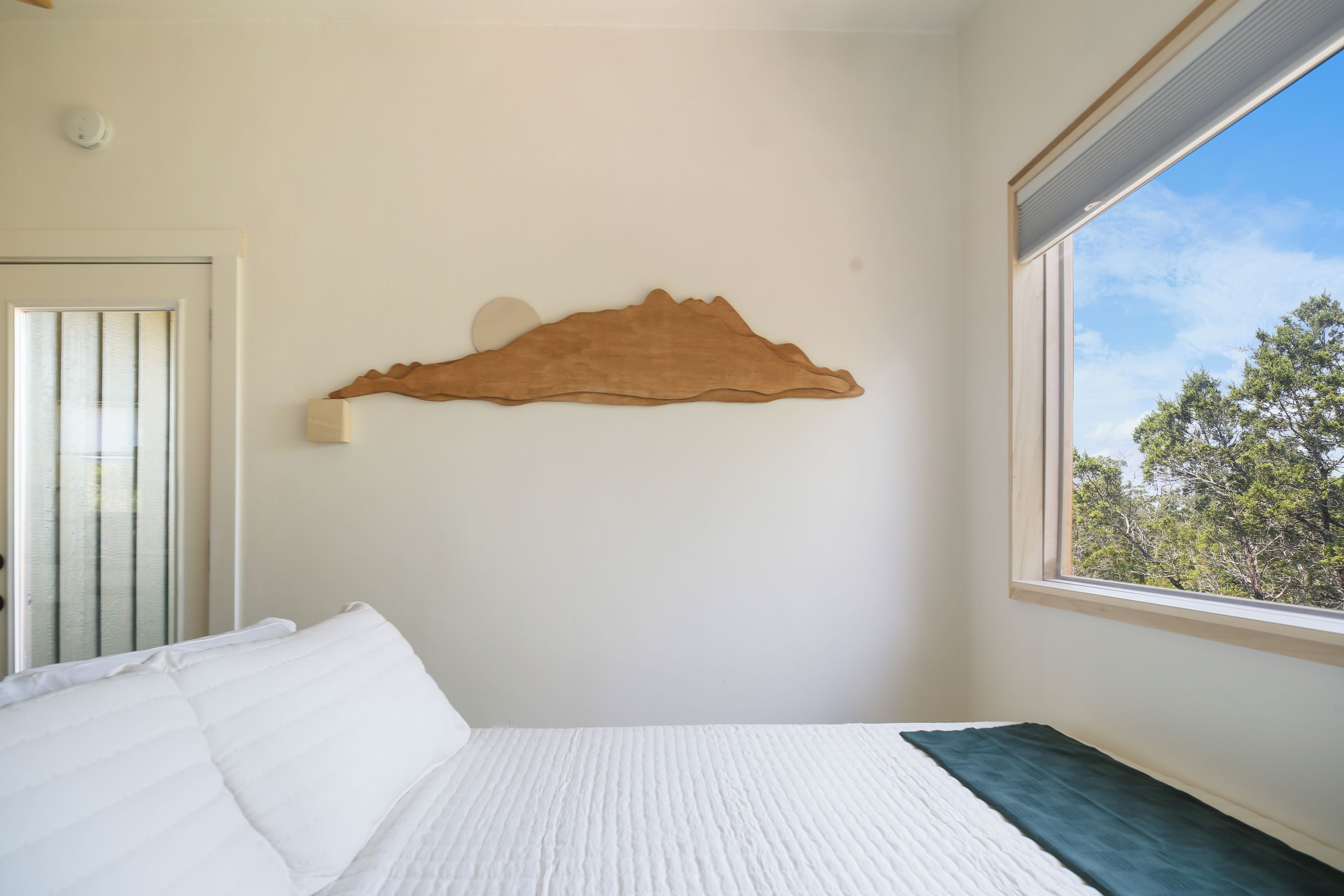 Una camera da letto con un letto, un'opera d'arte in legno a parete, una finestra e una porta.