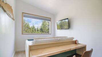 A room with a bed, a desk, a chair, a window with a view of trees, and a mounted television.