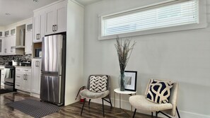 A modern kitchen with white cabinetry, a stainless steel refrigerator, and a built-in oven. There are two chairs with patterned cushions and a small table with a vase. - Home Away From Home - Surrey (Surrey)