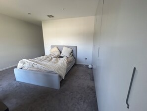 Un dormitorio moderno con cama, mesita de noche, estante en la pared y toma de corriente.