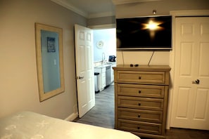 A bedroom with a bed, a dresser, a television mounted on the wall, and a door leading to a kitchen. - Bridgepointe Lake Escape (Osage Beach)