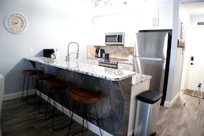 A modern kitchen with a marble island, bar stools, a stainless steel refrigerator, and a microwave. - Bridgepointe Lake Escape (Osage Beach)