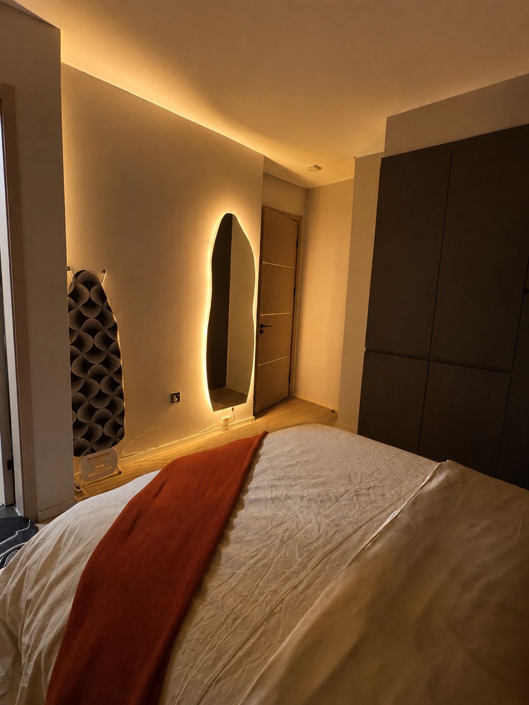 A bedroom with a bed, a bedside table, a mirror, and a wardrobe.