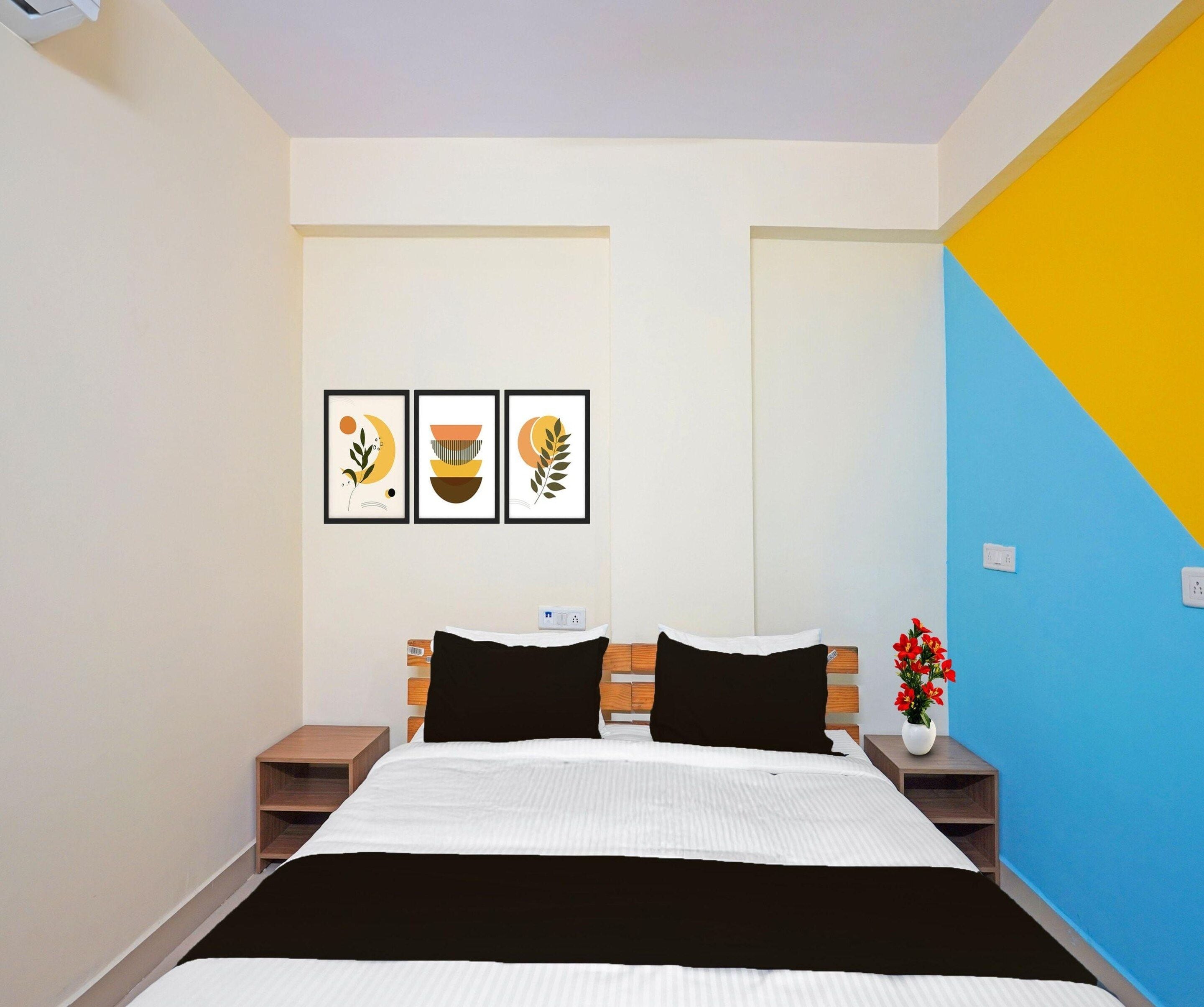 Une chambre à coucher comprenant un lit, deux tables de chevet, une prise de courant fixée au mur et trois œuvres d’art encadrées accrochées au mur.