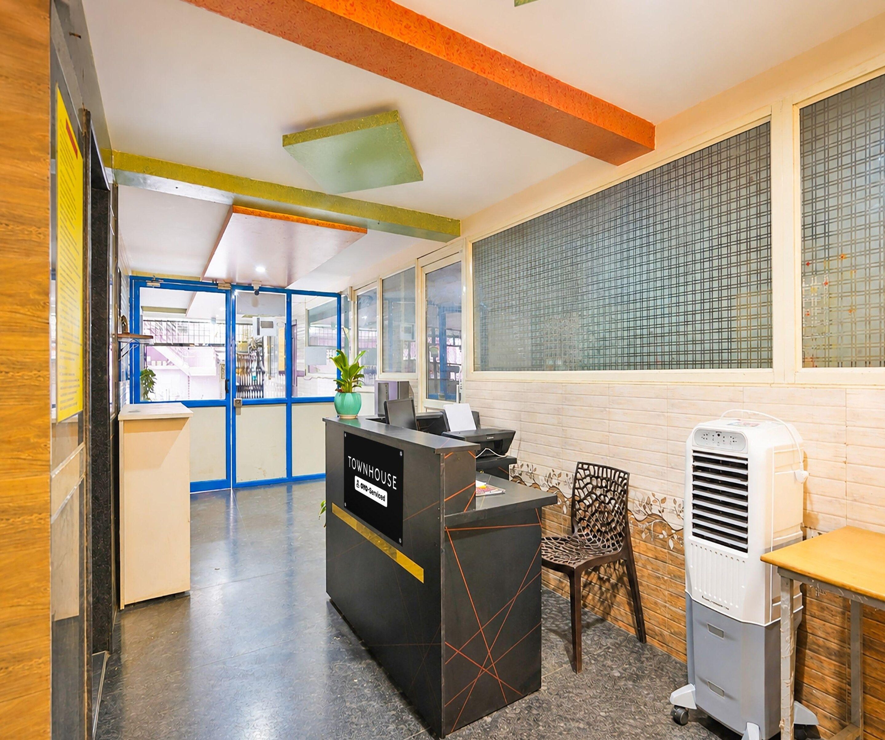 A reception desk with a sign reading 'TOWNHOUSE' and a phone number. There is a chair and a table with a white air conditioner.