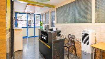 A reception desk with a sign reading 'TOWNHOUSE' and a phone number. There is a chair and a table with a white air conditioner.