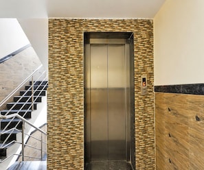 An elevator with a stone wall design, a digital display, and a wooden panel on the right. - Deluxe Room Nagawara Junction (Bengaluru)