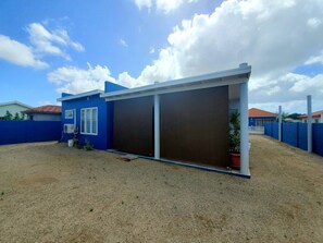 En bostadsbyggnad med en stor garageport, en inhägnad trädgård och en klar himmel.