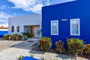 A modern two-story building with a blue exterior, a front entrance, and a small porch area. - Modern Relaxing Vacation Villa (Oranjestad)