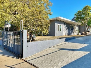 A residential property with a gated entrance, a concrete driveway, and a house with a flat roof and a small porch.