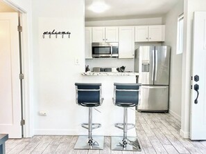 A modern kitchen with white cabinets, stainless steel appliances, and two bar stools.