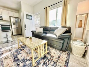 A living room with a sofa, a coffee table, a rug, and a kitchen area with appliances.