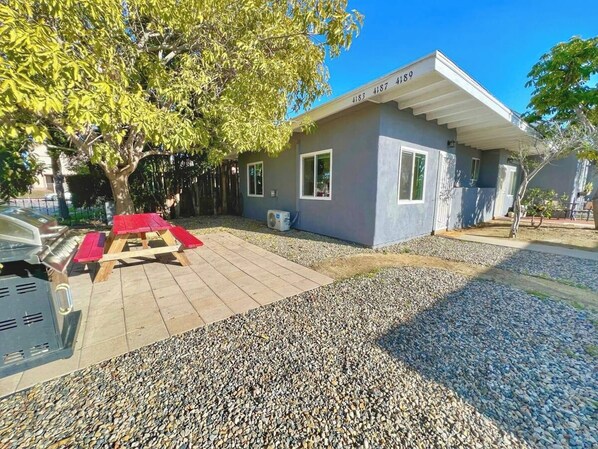 A small building with a number 4183 4187 4189 on the facade, a gravel driveway, and a red bench.