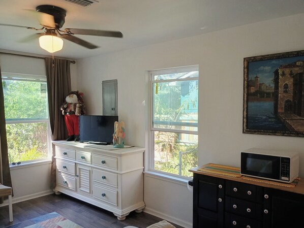 A room with a ceiling fan, a dresser with drawers, a television, a microwave, and a painting on the wall. - Private apartment in downtown Tallahassee. Private entrance. Access to backyard. (Tallahassee)