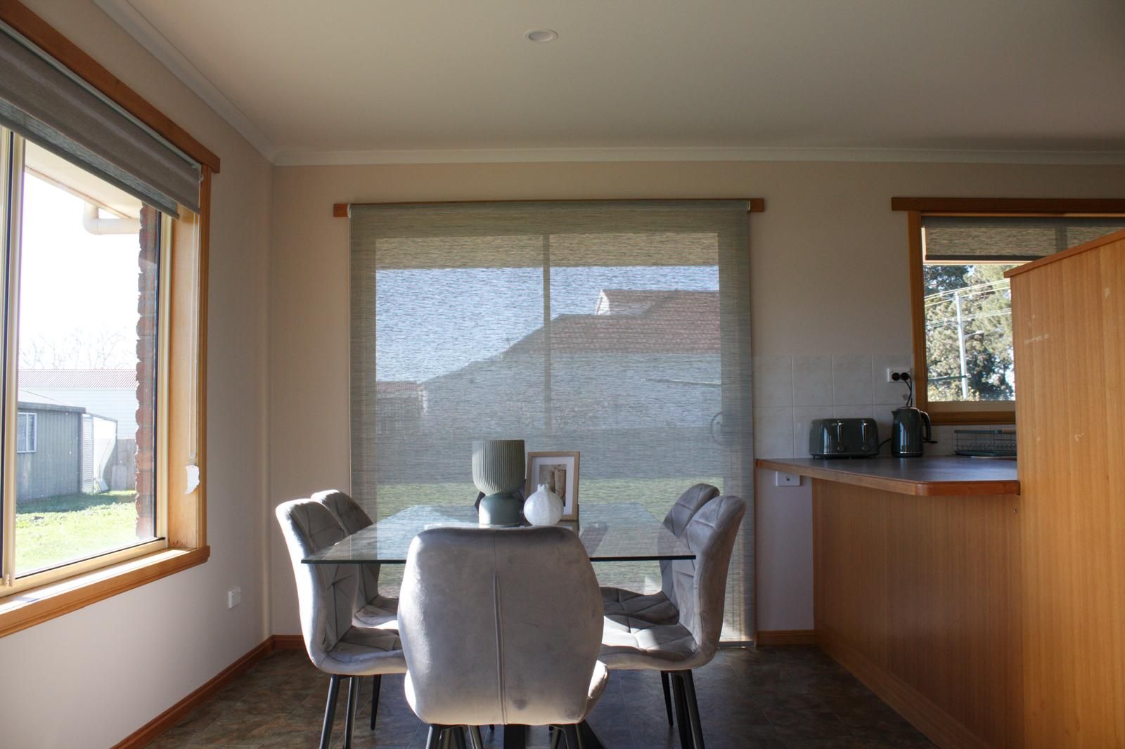 A dining area with a table and chairs, a window with blinds, and a kitchen area with a counter and appliances.