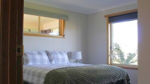 A bedroom with a bed, a bedside lamp, a window with a view, and a mirror above the bed. - Quaint Country Home (Westbury)