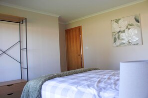 Un dormitorio con una cama, una puerta de madera, un cuadro colgado en la pared y una estantería metálica.