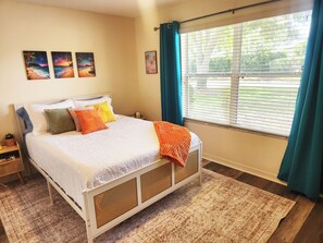 Ein Schlafzimmer mit Bett, einem Fenster mit Vorhängen und Wandbildern.