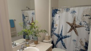A bathroom with a sink, toilet, and shower curtain featuring marine life. - Coastal Breeze Getaway 2BR/2BA BBQ + Fire Table + Lanai + Garage (The Villages)