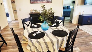 A dining area with a round table, black chairs, a striped tablecloth, and a blue vase with a plant. - Coastal Breeze Getaway 2BR/2BA BBQ + Fire Table + Lanai + Garage (The Villages)