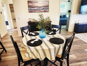Un coin repas avec une table ronde, des chaises noires, une nappe à rayures et un vase bleu contenant une plante.