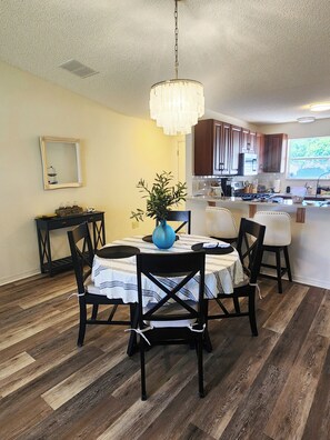 A dining area with a round table, chairs, a vase, and a chandelier. - Coastal Breeze Getaway 2BR/2BA BBQ + Fire Table + Lanai + Garage (The Villages)