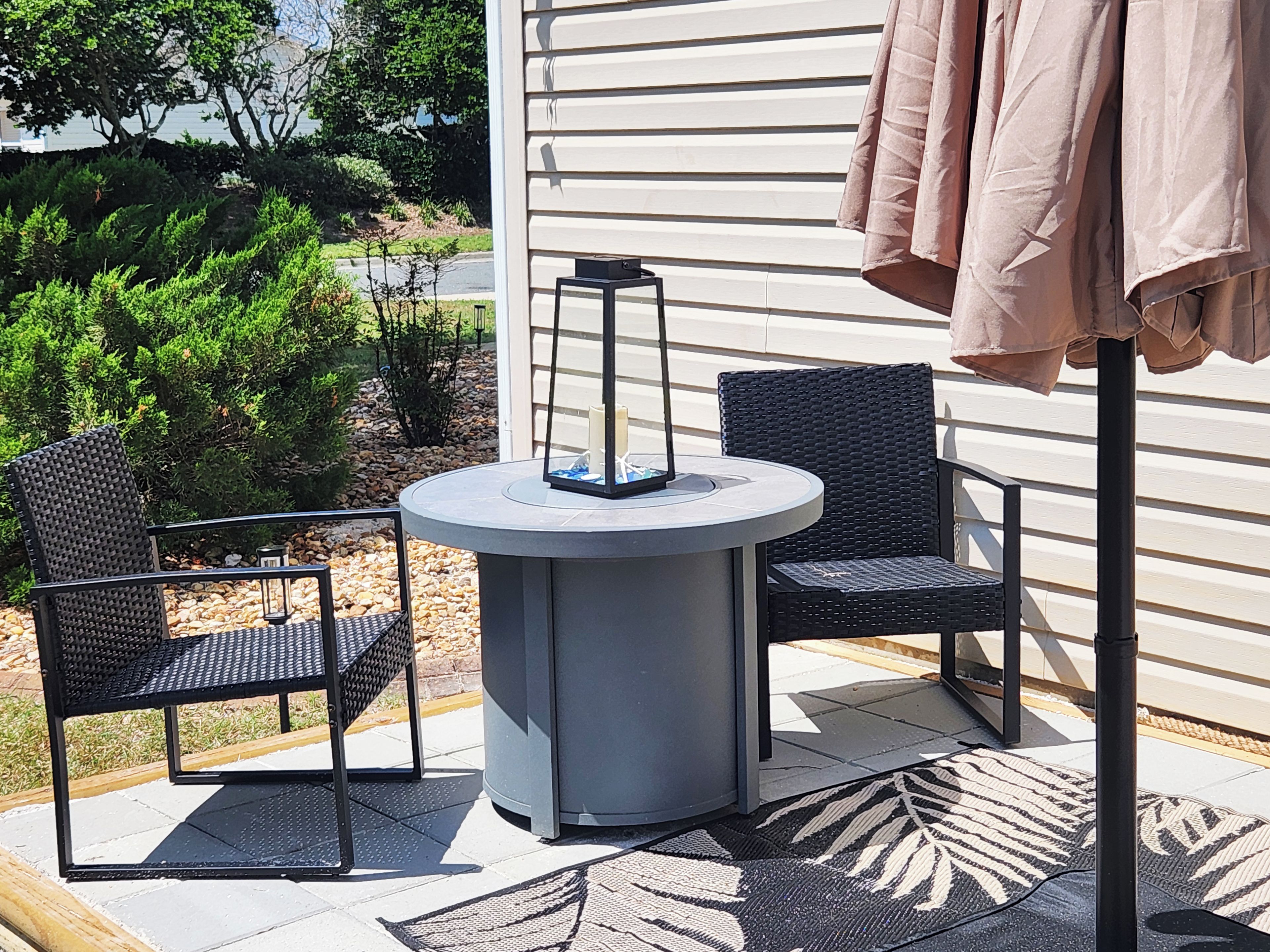 Une terrasse extérieure avec une table ronde et deux chaises, une lanterne et une pergola surmontée d’une toiture marron.