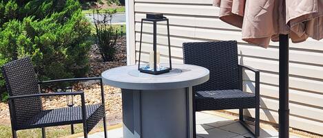 Une terrasse extérieure avec une table ronde et deux chaises, une lanterne et une pergola surmontée d’une toiture marron.