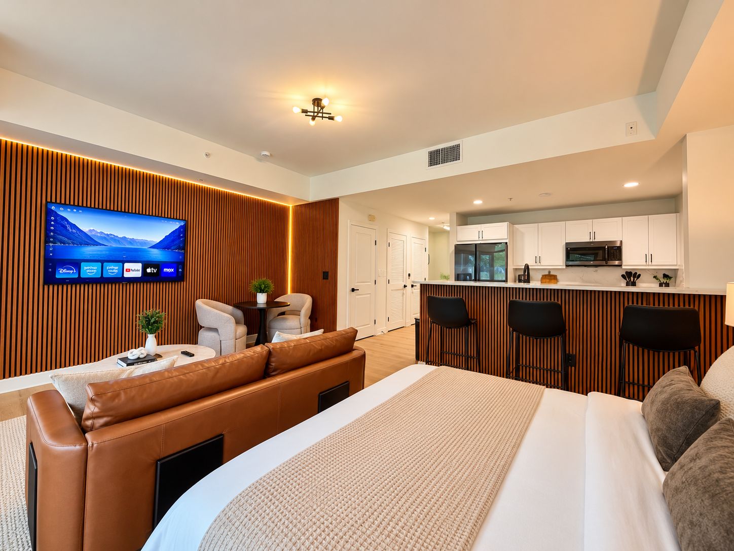 Une chambre d’hôtel moderne dotée d’un grand lit, d’un coin salon avec télévision et d’une kitchenette.