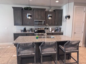 A modern kitchen with dark wood cabinets, a granite countertop, and a central island with chairs. - Peaceful Poolside Perfection!  4 bedroom 3-with King Beds & ensuites, 4-1/2 bath (Washington)