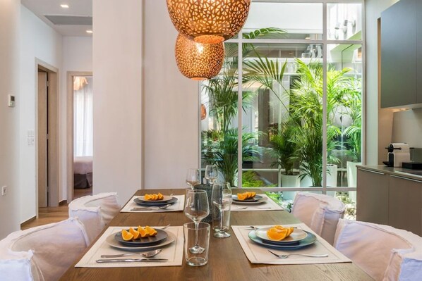 Comedor con una mesa preparada para cuatro, lámpara colgante y vista a plantas de interior a través de una ventana.