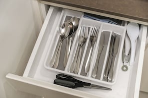 Un cajón con cubiertos ordenados, incluyendo cucharas, tenedores, cuchillos y un par de tijeras.
