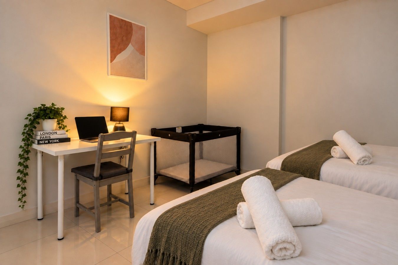 Habitación de hotel con escritorio, silla, ordenador portátil, dos camas con toallas, una mesita pequeña y una planta.