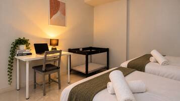 Habitación de hotel con escritorio, silla, ordenador portátil, dos camas con toallas, una mesita pequeña y una planta.