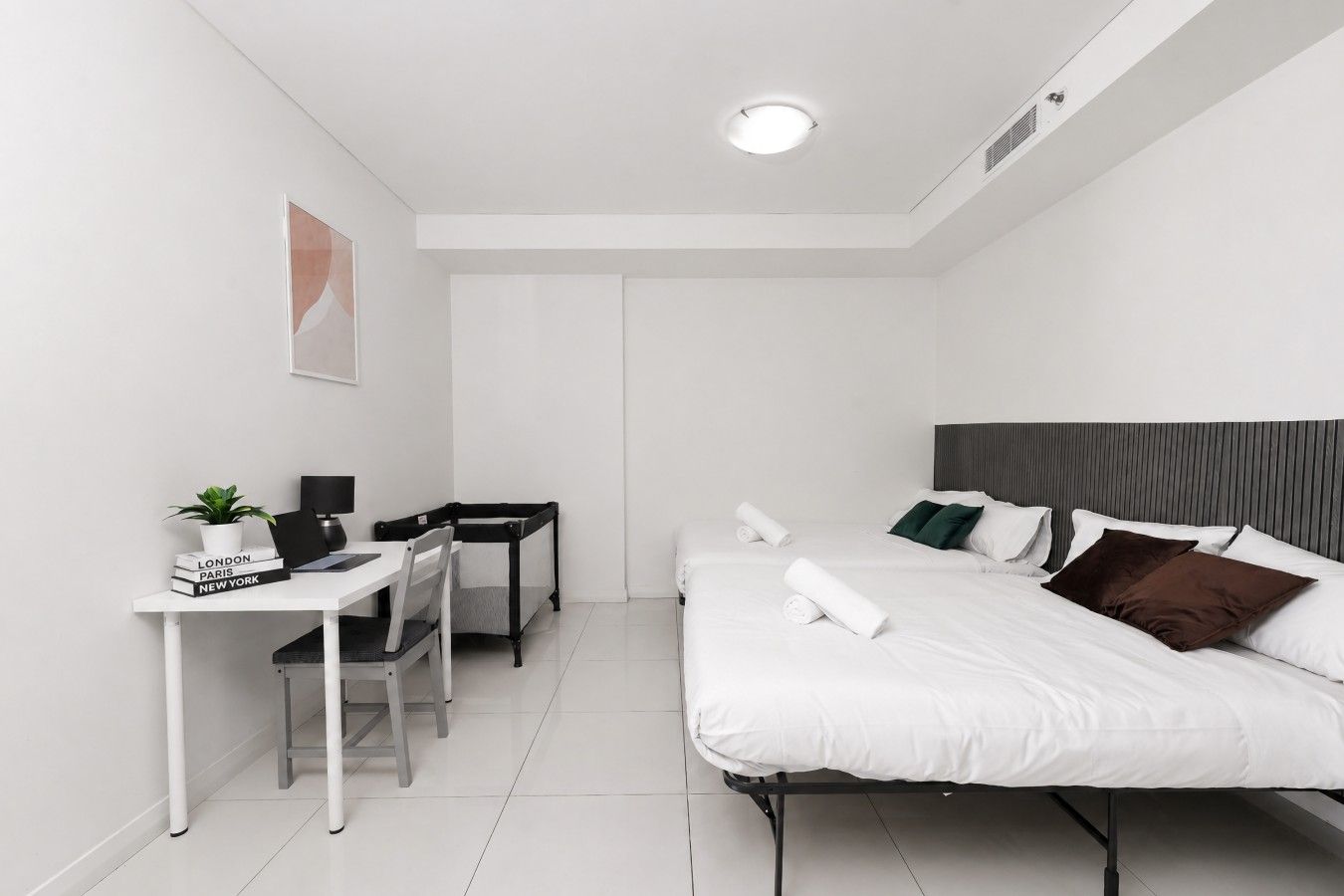 Ein modernes Hotelzimmer mit Bett, Schreibtisch, Stuhl und einem kleinen Tisch mit Pflanze und Büchern.