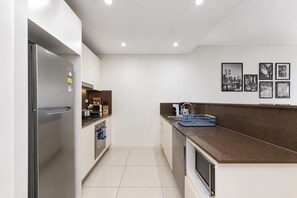 A modern kitchen with a stainless steel refrigerator, a stove, and a sink. There are framed pictures on the wall and a blue dish rack on the counter. - Free parking near Sydney Airport with balcony (Mascot)