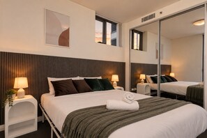 A hotel room with a large bed, two bedside tables with lamps, a mirror, and a wall-mounted artwork. - Free parking near Sydney Airport with balcony (Mascot)