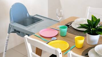 Un comedor con una mesa preparada para dos personas, con platos, cubiertos y una copa.