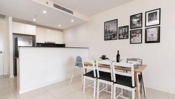 Una cocina moderna con armarios blancos, un comedor con mesa y sillas de madera, y una pared decorada con cuadros.
