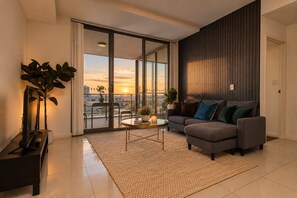 A modern living room with a sofa, a coffee table, and a view of the city at sunset. - Free parking near Sydney Airport with balcony (Mascot)