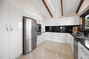 A modern kitchen with white cabinetry, a stainless steel refrigerator, and a black countertop. - Cedar By The Sea—Beach, River & Golf Getaway (Goolwa South)
