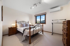 A bedroom with a bed, bedside tables, a dresser, a window with a view, and an air conditioning unit. - Cedar By The Sea—Beach, River & Golf Getaway (Goolwa South)