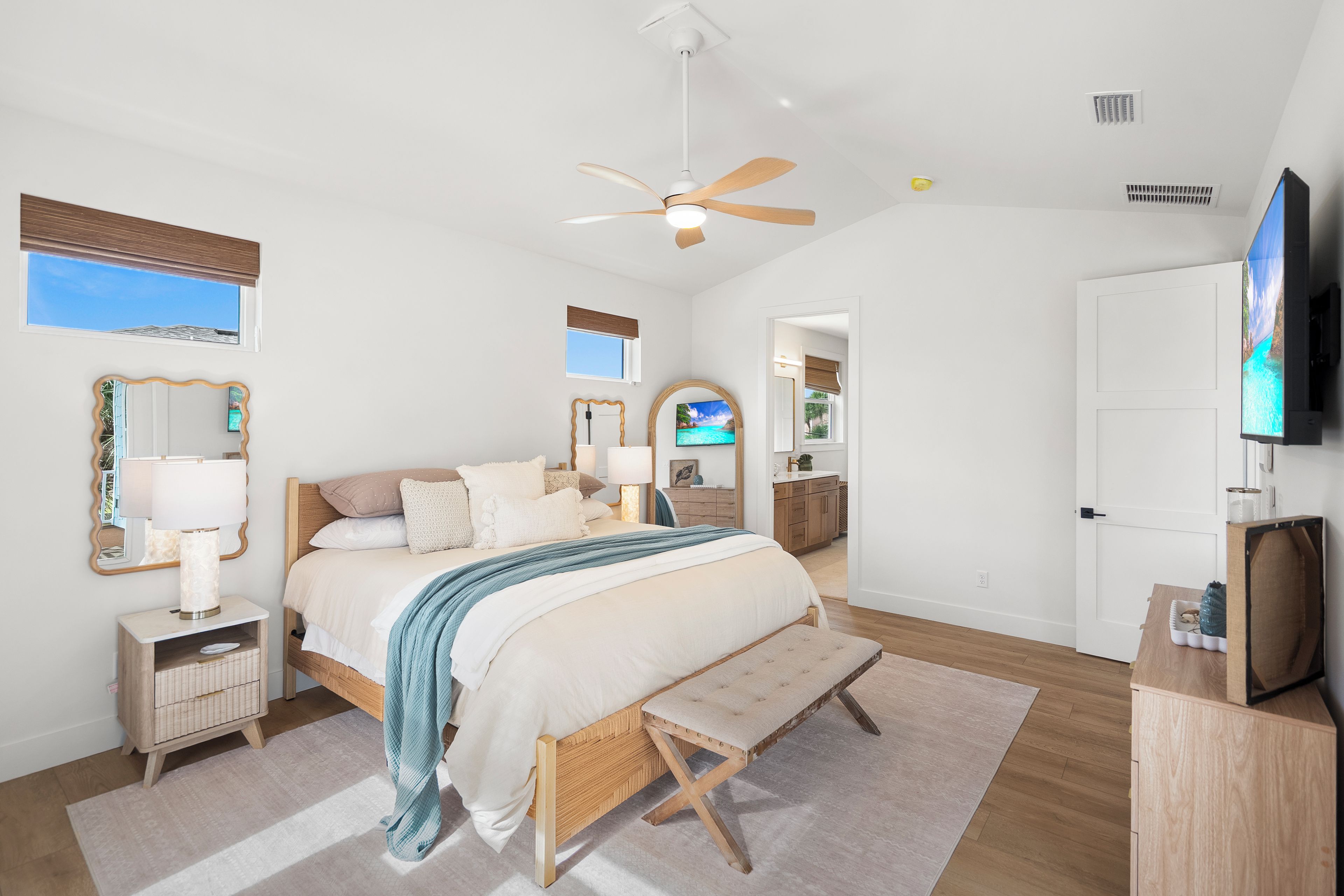A modern bedroom with a bed, bedside tables, a ceiling fan, a TV, and a view of the outdoors.