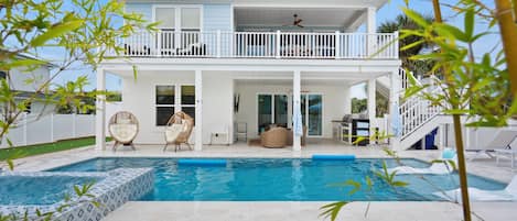 A two-story house with a pool, white exterior, and a balcony with a ceiling fan.