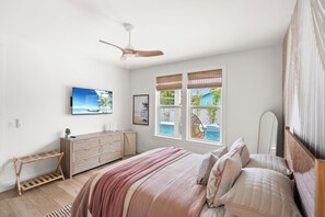 Ein Schlafzimmer mit einem Bett, einem Schminktisch, einem Fernseher und einem Fenster mit Blick auf einen Pool.