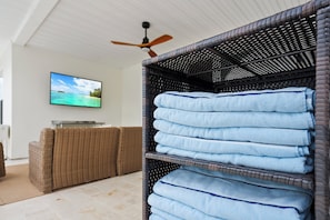Ein Zimmer mit einem Korbsessel, einem Fernseher, der eine Strandansicht zeigt, und einem Regal mit gefalteten Handtüchern.